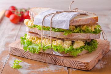 Sandwich with scramble eggs, leaves salad and ham on wooden baskgraund. Selective focus