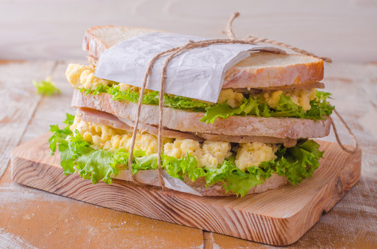 Sandwich with scramble eggs, leaves salad and ham on wooden baskgraund. Selective focus