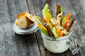 Grilled chicken wings with creamy sauce for dipping with a glass filled with sliced fresh vegetable 