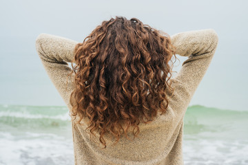 Curly brunette in a sweater on the coast faces the sea and strai