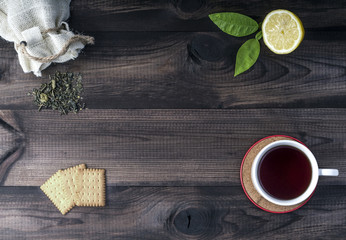 cup of tea with fresh lemon, tea cookies and linen bag with green tea leaves on wooden table.