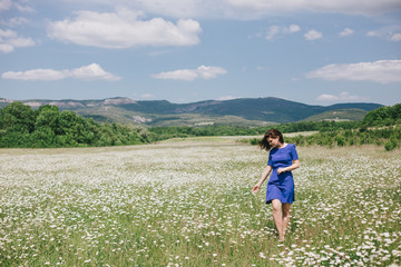 Naklejka na ściany i meble Young beautiful woman in a blue dress enjoying chamomile field among mountains. Summer mood