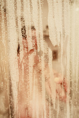 Unfocused portrait of a woman showering through the bath screen