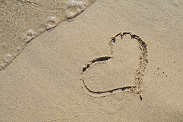 Heart drawn on the sand of beach with sea foam and wave