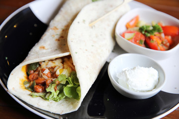Mexican burritos on a plate with tomato salad