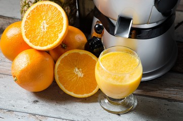 Juicer and orange juice in glass on wooden desk