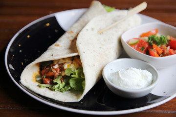 Mexican burritos on a plate with tomato salad