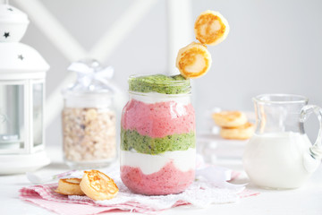 Smoothie with cottage cheese, strawberries and spinach in a glass jar with small cheese pancakes on a white table. Selective focus.