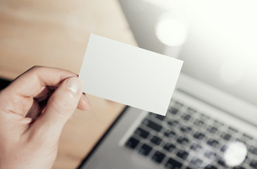 Obraz premium Closeup Photo Man Showing Blank White Business Card and Using Modern Laptop.Wood table Blurred Background. Mockup Ready for Private Information.Sunlight Reflections Screen Gadget. Horizontal mock up.
