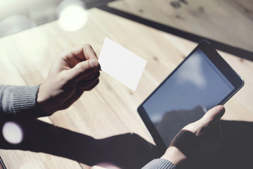 Photo Man Showing Blank White Business Card, Holding Hand Modern Digital Tablet.Wood table Blurred Background.Mockup Ready  Private Information.Sunlight Reflections Screen Gadget.Horizontal mock up.