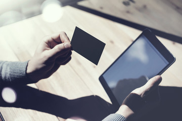 Photo Man Showing Blank Black Business Card, Holding Hand Modern Digital Tablet.Wood table Blurred Background.Mockup Ready  Private Information.Sunlight Reflections Screen Gadget.Horizontal mock up.