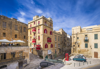 Fototapeta na wymiar Malta, Valletta - Ancient maltese houses with traditional red balconies and windows and red telephone box