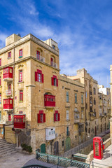 Fototapeta na wymiar Malta, Valletta - Streetview with traditional red balconies and windows and red telephone box