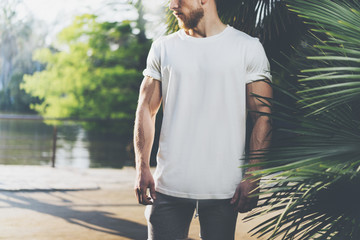 Photo Bearded Muscular Man Wearing White Blank t-shirt in summer time. Green City Garden, lake and palms Background,blurred. Horizontal Mockup