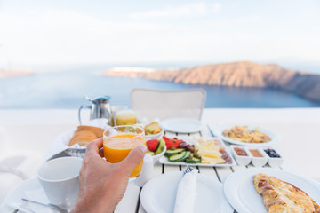 European vacation healthy breakfast food selfie. POV of man drinking morning orange juice at resort restaurant. Table for two on outdoor hotel balcony caldera view on Oia Santorini, Greece, Europe.