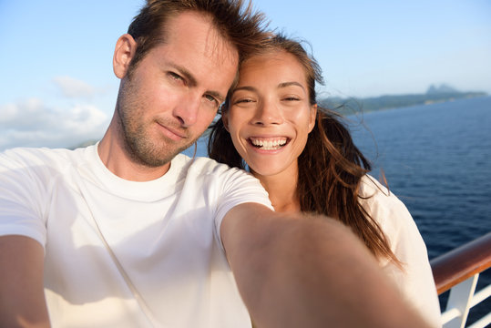 Selfie couple taking holiday self-portrait picture of themselves. Happy multiracial friends having fun together on cruise vacation in Caribbean destination taking smartphone photos as summer memories.
