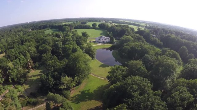 Drone aerial bird eye helicopter view of beautiful classic luxury real estate white house villa mansion and later flying over a small farm through and over trees green field and crisp blue sky 4k