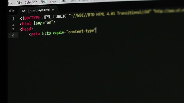 Shallow DOF shot of a computer screen while programmer was writing basic html page code, some basic tags and Hello World! message can be read, other code is blurry