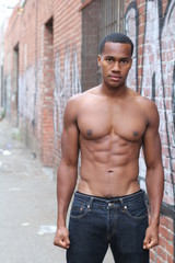 Fototapeta premium One amazing African man with muscular male sensual topless body with strong cool 6 pack abdominal and athletic chest dressed in just jeans posing on graffiti wall background