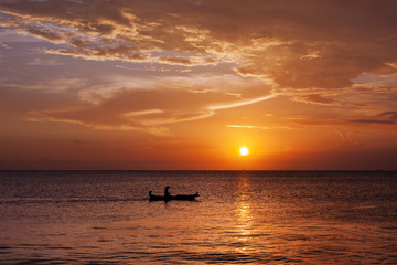 Naklejka na ściany i meble Man in boat witnessing a magical golden sunset in Bali, Indonesia 