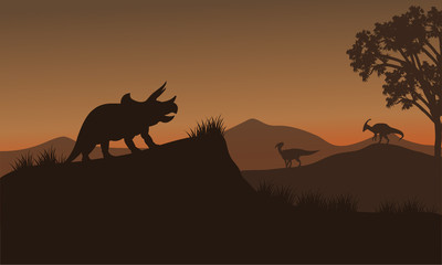 Fototapeta na wymiar Triceratops and Eoraptor silhouette in hills