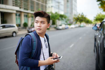Portrait of Vietnamese young photographer with smartphone standing in street