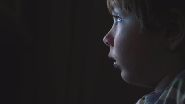 Young boy watching cartoons in a dark room on a computer
