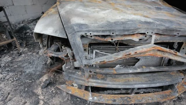 pan footage of burned out car in garage after fire, grunge apocaliptic scene