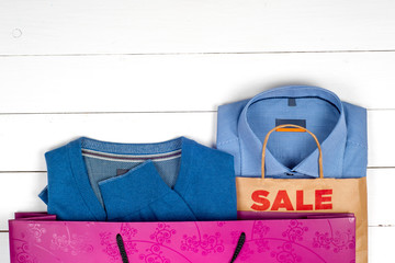 blue shirt and sweater for men  with bags in the sales on wooden white background.