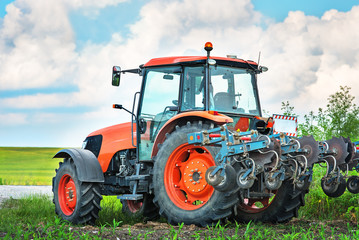 Modern red tractor on the agricultural field.