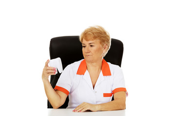Smile elderly female dentist sitting behind the desk and holds big tooth model