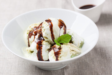 Vanilla and pistachio ice cream with chocolate sauce in a bowl on a plate on a linen textile, closeup
