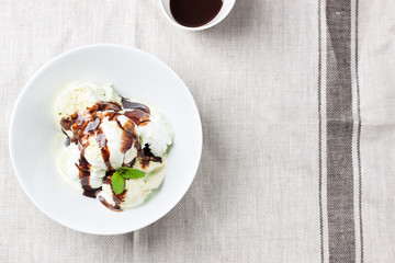Vanilla and pistachio ice cream with chocolate sauce in a bowl on a plate on a linen textile, top view