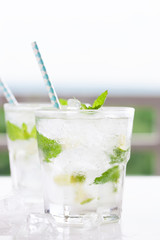 Non alcohol cold mojito cocktail with fresh lime, mint and crushed ice on a white plate, closeup.