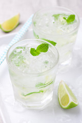 Non alcohol cold mojito cocktail with fresh lime, mint and crushed ice on a white plate, closeup.