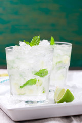 Non alcohol cold mojito cocktail with fresh lime, mint and crushed ice on a white plate, closeup