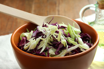 chopped cabbage in a brown bowl with a wooden spoon near oil on a wooden table