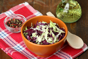 chopped cabbage in a brown bowl with a wooden spoon near oil and lots of spices on the cloth on a wooden table