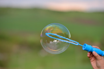 Close up of a soap bubble growing from the blower ring hold by a