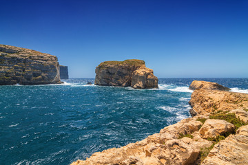 Fototapeta na wymiar Surging waves break on the rocky shore of Dwejra bay in Gozo, Malta.