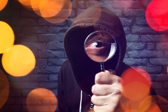 Hooded computer hacker with magnifying glass