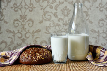A glass and a bottle of milk, a loaf of bread and a towel