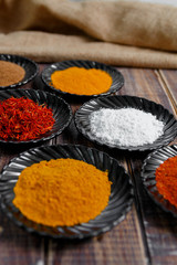 Spices in black ceramic plates on wooden background. Various spices selection. Six plates with different colorful spices