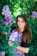 Portrait of Beautiful, long haired, dark-haired girl in purple dress in blooming trees. Attractive romantic woman in flowers of lilac. Warm photo.