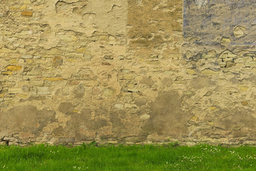 Hintergrund – Natursteinwand mit sich ablösendem Putz und Wiese im Frühling