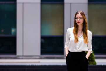 beautiful slim girl sexy on the background of strict building in the style of the office holds glasses. Portrait