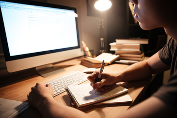 Man writing at notepad and using computer in dark room
