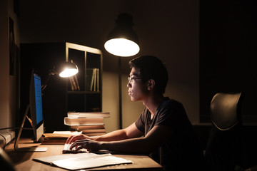 Serious man using computer and typing in dark room