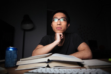 Thoughtful man in glasses studying using books and computer