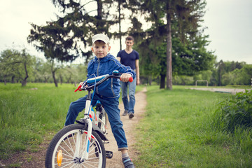 Fototapeta premium Small boy riding a bike together with his father